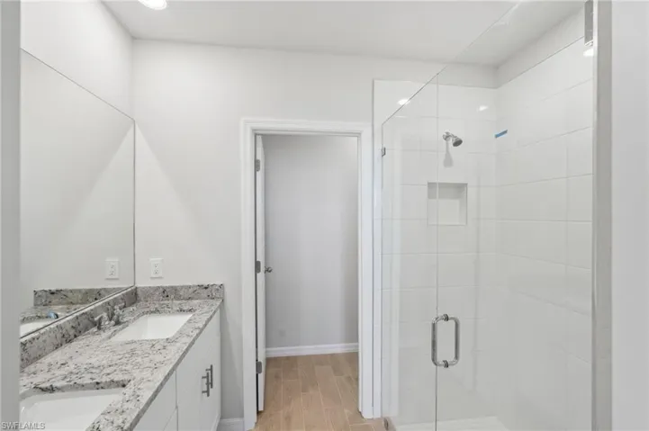 Bathroom with a stall shower, double vanity, a sink, and baseboards