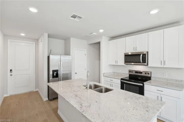 Kitchen featuring visible vents, appliances with stainless steel finishes, a kitchen island with sink, a sink, and baseboards