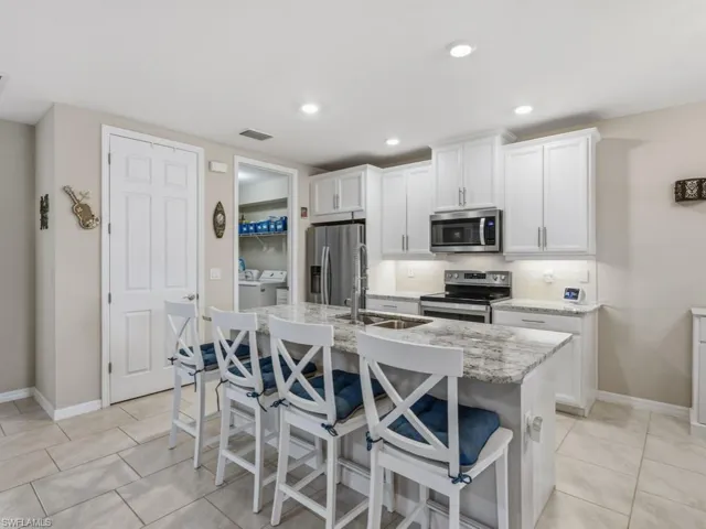 Kitchen with white cabinetry, a breakfast bar area, stainless steel appliances, granite countertops, pantry and a kitchen island with sink