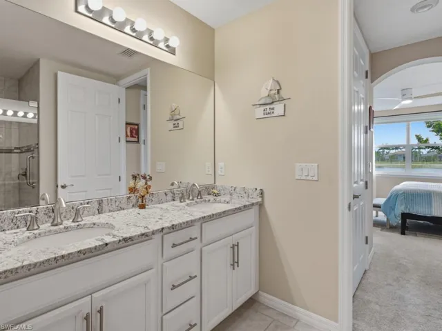 Full bath featuring double vanity, ensuite bathroom, matching tile, and a tile shower with grab bars for safety