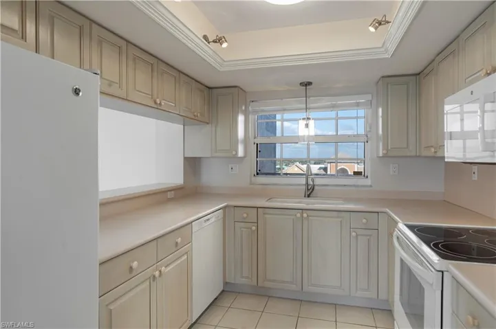 Kitchen with white appliances, a sink, hanging light fixtures, light countertops, and a raised ceiling