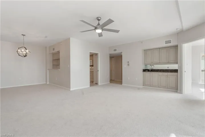 Unfurnished living room with light colored carpet, visible vents, baseboards, and ceiling fan with notable chandelier