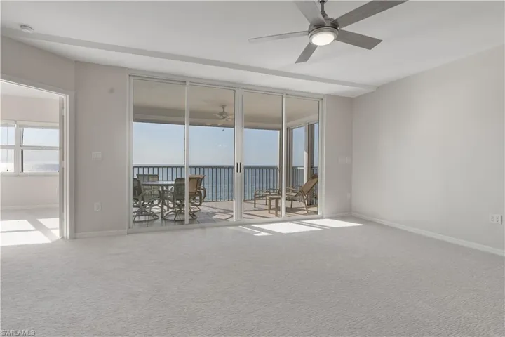 Unfurnished room with a ceiling fan, a water view, light carpet, and baseboards