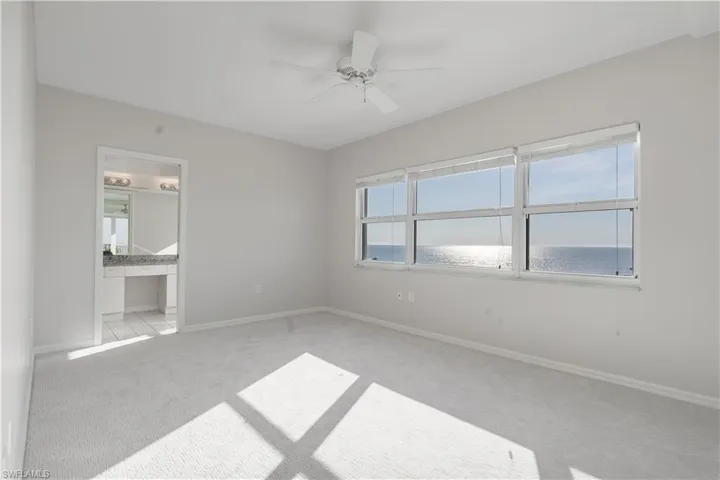 Empty room featuring baseboards, a water view, a ceiling fan, and light colored carpet