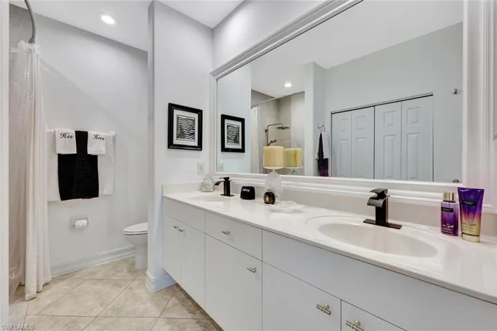 Full bathroom with double vanity, a shower with curtain, tile patterned floors, and a closet