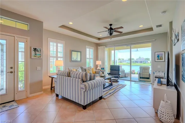 Living area featuring light tile patterned floors, a raised ceiling, ceiling fan, and recessed lighting