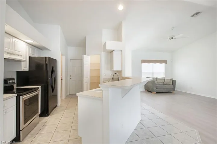 Open-concept living area featuring a kitchen with white cabinetry and stainless steel appliances