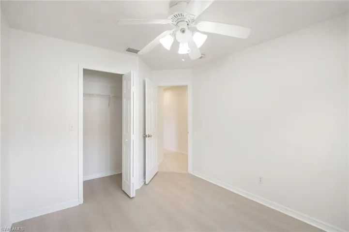 Bright room featuring a ceiling fan with integrated lighting, clean white walls, and light wood-finish flooring
