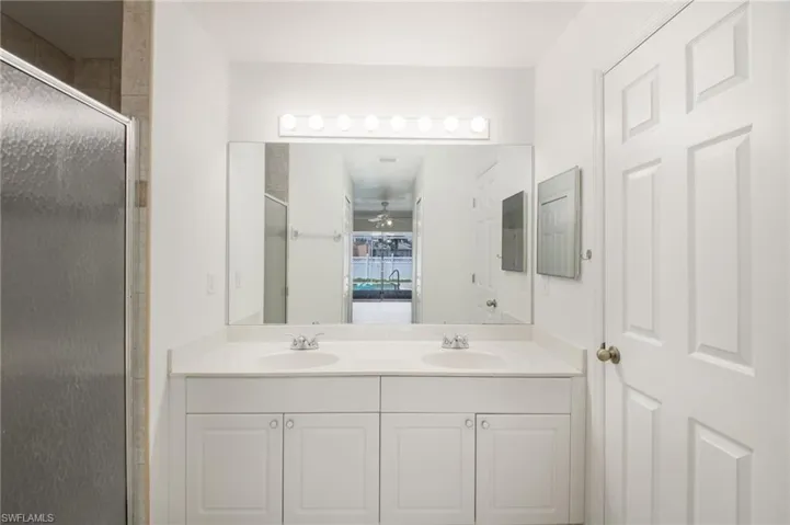 Bathroom featuring a dual vanity with white cabinetry and integrated sinks, a large wall-mounted mirror, and overhead strip lighting