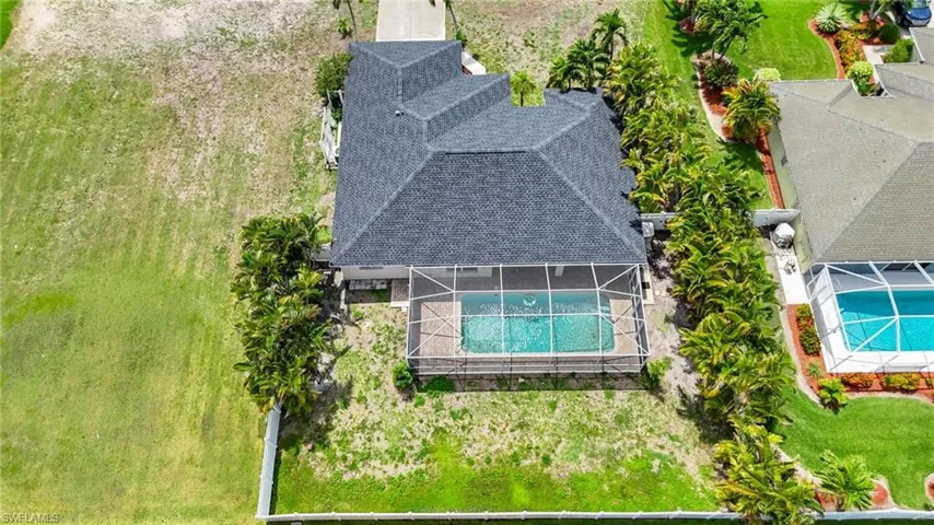 Aerial view of a residential property featuring a screened-in swimming pool and a dark shingle roof