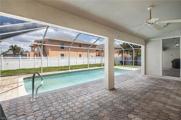 Screened-in patio area featuring a rectangular swimming pool with a handrail, paver decking, and a ceiling fan