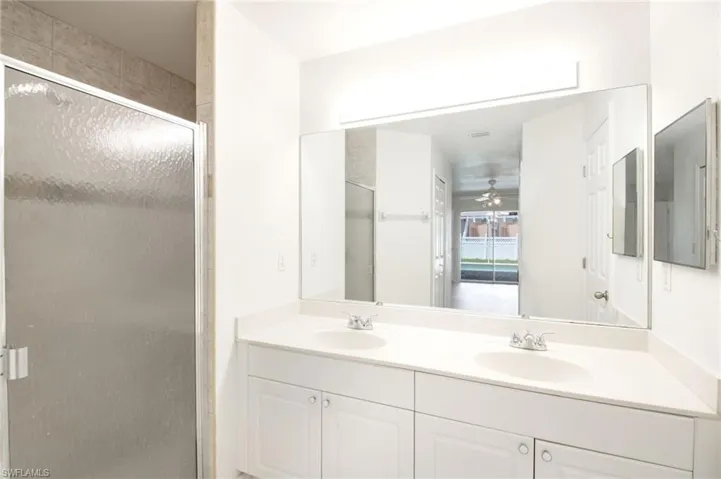 Bathroom featuring a dual vanity with built-in sinks, a large wall-mounted mirror, and a glass-enclosed shower with tiled walls