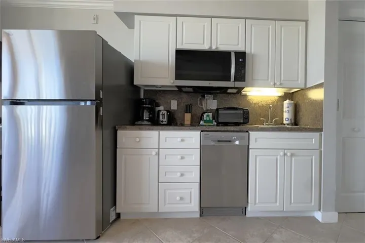 Kitchen with stainless steel appliances, white cabinetry, dark stone countertops, backsplash, and light tile patterned flooring