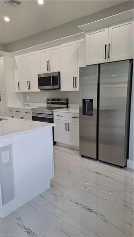 Kitchen featuring fridge, stove, recessed lighting, light marble finish floors, and white cabinetry