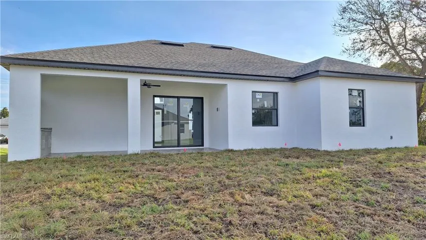 Back of property with a shingled roof, ceiling fan, a lawn, and stucco siding
