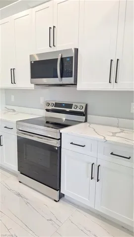 Kitchen featuring electric range, light marble finish floors, white cabinets, and light stone counters