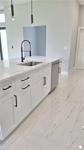 Kitchen with dishwashing machine, a sink, light marble finish floors, light stone countertops, and white cabinets