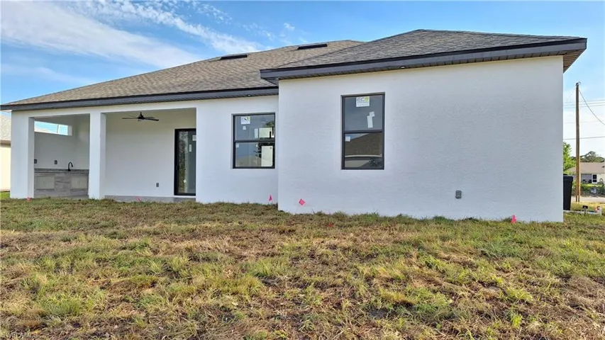 Back of property featuring stucco siding, ceiling fan, a shingled roof, and a yard