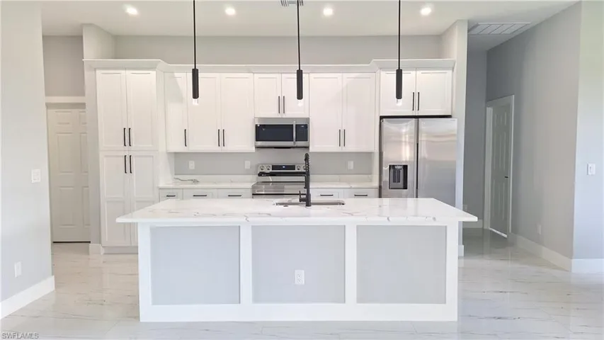 Kitchen featuring stainless steel appliances, baseboards, a sink, an island with sink, and light marble finish flooring