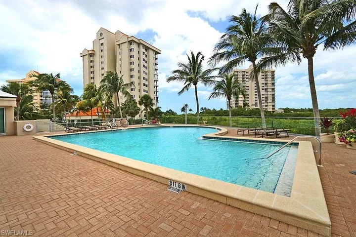 Expansive outdoor swimming pool with integrated spa, surrounded by a brick paver deck and tropical landscaping
