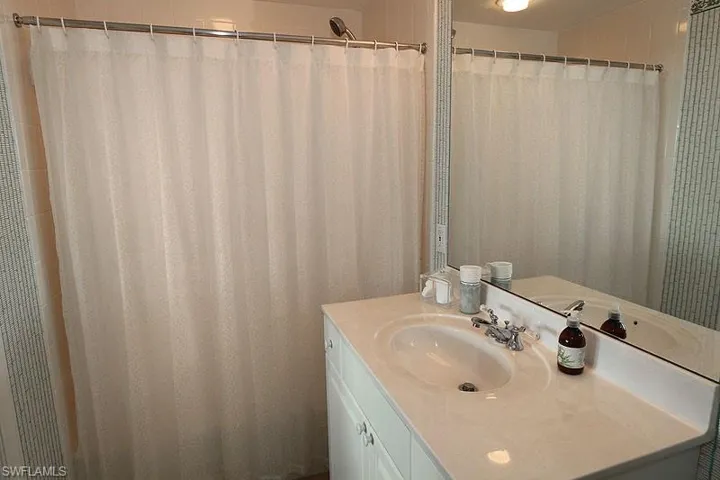 Bathroom featuring a vanity with an integrated sink and chrome fixtures, a full-width wall mirror, and a shower with a privacy curtain