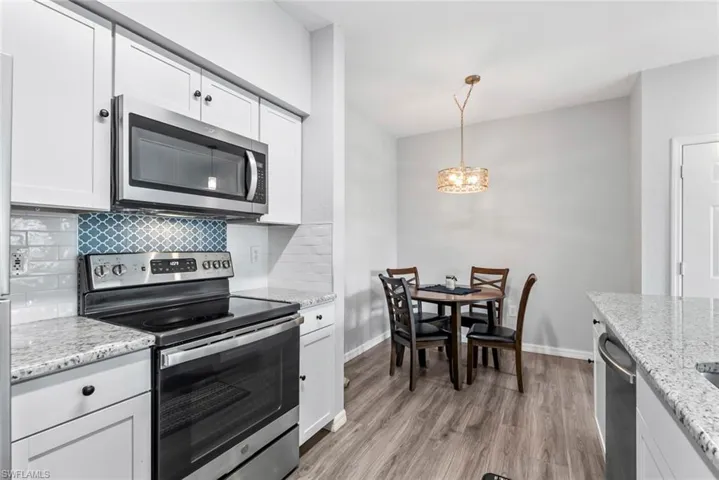 Kitchen with an inviting chandelier, stainless steel appliances, decorative backsplash, light wood finished floors, and white cabinets
