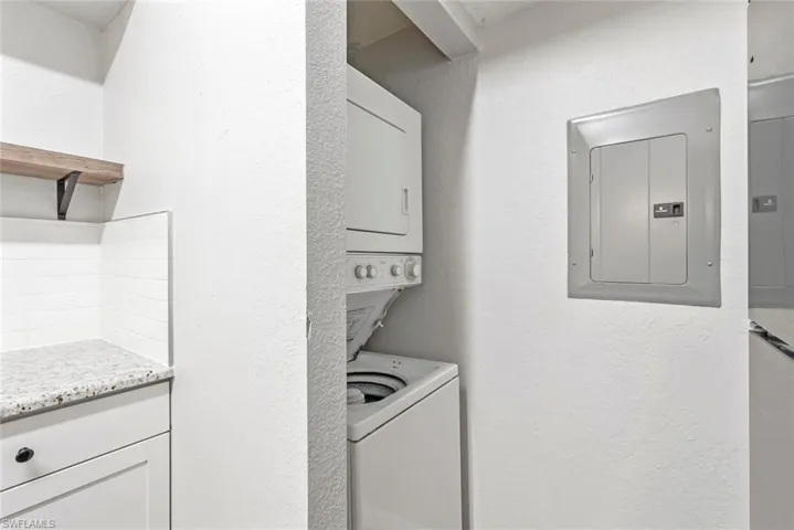 Washroom with a textured wall, stacked washing maching and dryer, laundry area, and electric panel