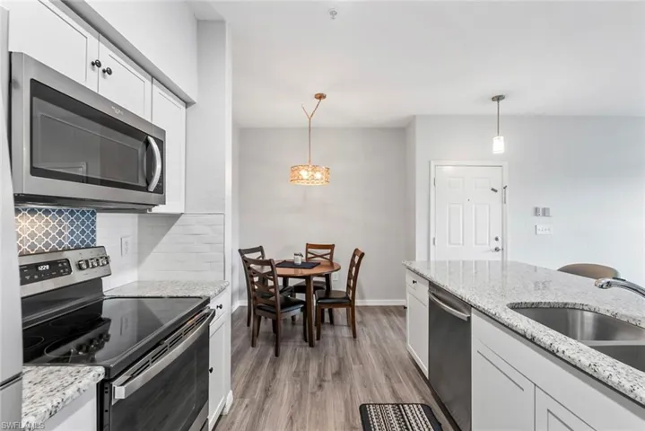 Kitchen with pendant lighting, light wood finished floors, tasteful backsplash, stainless steel appliances, and white cabinets