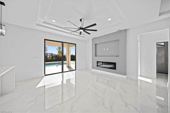 Unfurnished living room featuring a glass covered fireplace, recessed lighting, a ceiling fan, light marble finish flooring, and a raised ceiling