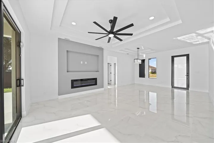 Unfurnished living room featuring recessed lighting, a ceiling fan, a glass covered fireplace, a raised ceiling, and light marble finish flooring