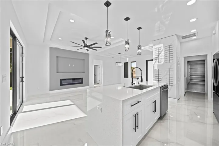 Kitchen with light stone counters, light marble finish flooring, white cabinets, an island with sink, and ceiling fan