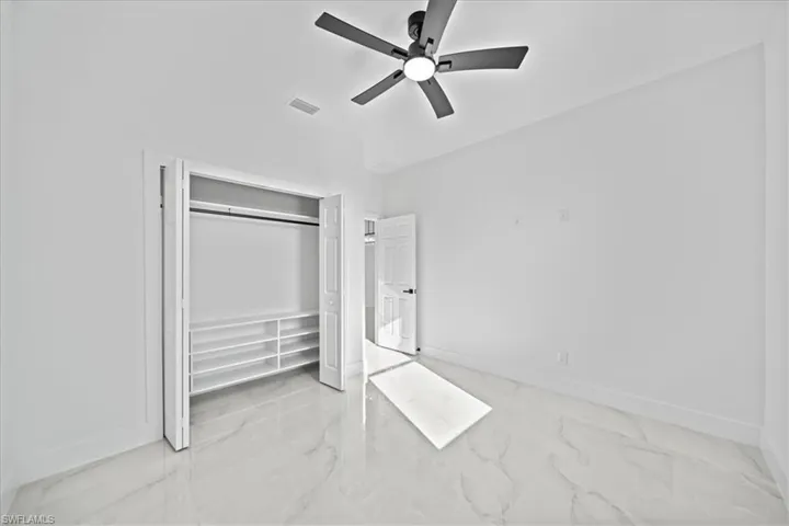 Unfurnished bedroom with light marble finish flooring, ceiling fan, and a closet