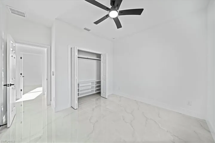 Unfurnished bedroom featuring light marble finish floors, a ceiling fan, and a closet