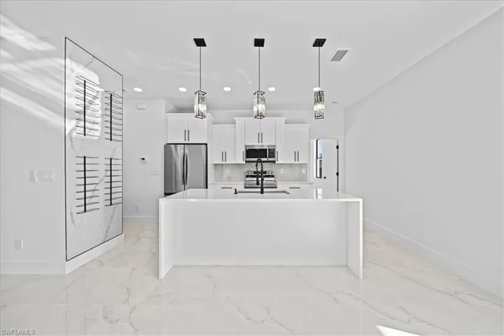 Kitchen featuring white cabinets, stainless steel appliances, a kitchen island with sink, light stone countertops, and hanging light fixtures