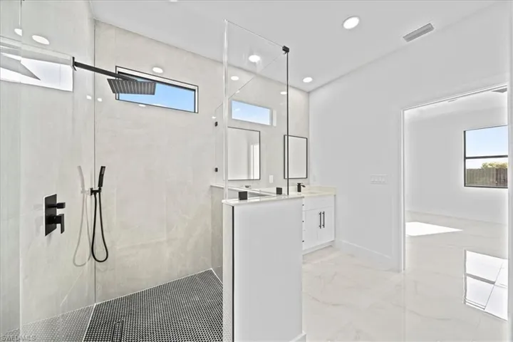 Full bath featuring vanity, a walk in shower, plenty of natural light, light marble finish flooring, and recessed lighting