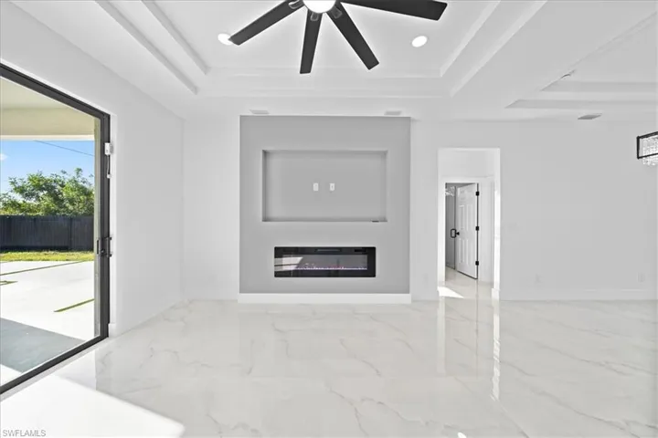 Unfurnished living room with a ceiling fan, a glass covered fireplace, a raised ceiling, and recessed lighting