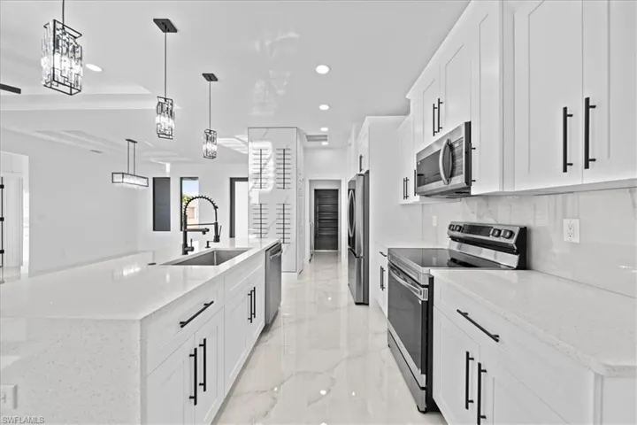 Kitchen featuring stainless steel appliances, white cabinets, light stone counters, a spacious island, and pendant lighting