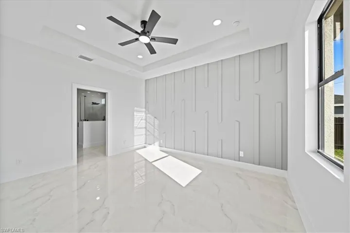 Unfurnished bedroom with multiple windows, a tray ceiling, light marble finish floors, a ceiling fan, and recessed lighting
