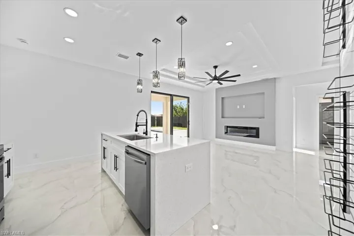 Kitchen with ceiling fan, light stone counters, a kitchen island with sink, open floor plan, and decorative light fixtures