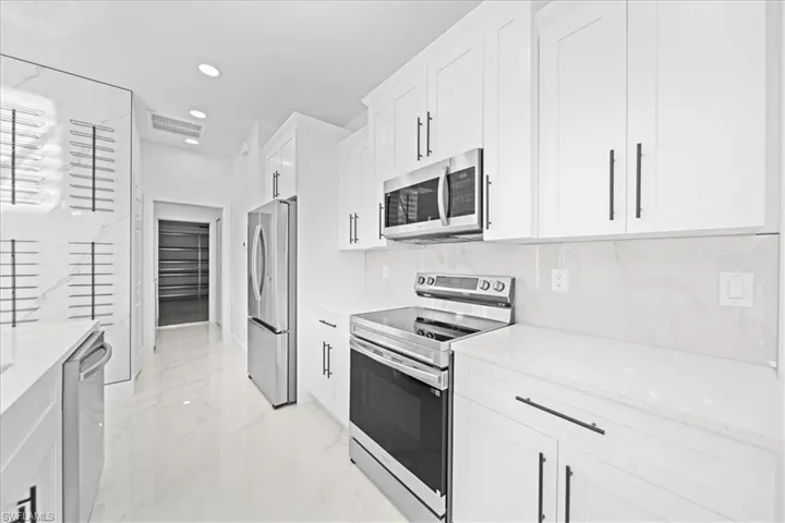 Kitchen featuring stainless steel appliances, white cabinetry, light stone countertops, recessed lighting, and light marble finish flooring