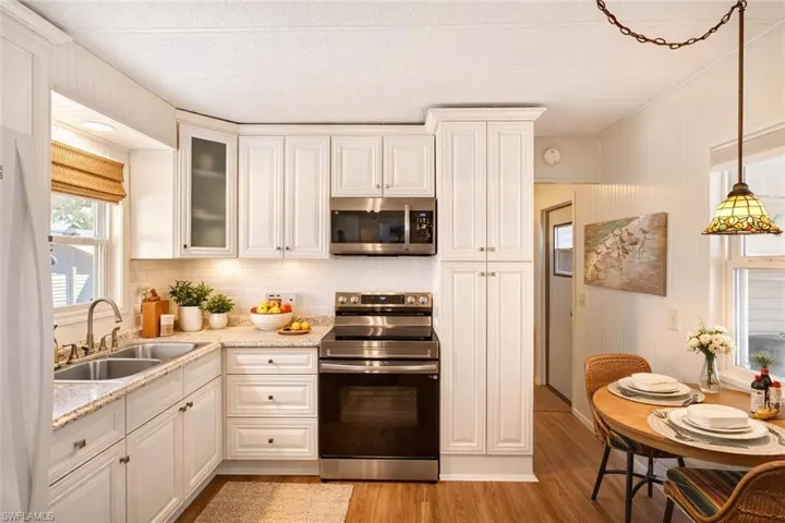 Kitchen with stainless steel appliances, light stone counters, glass fronted cabinets, light wood-style flooring, and white cabinetry