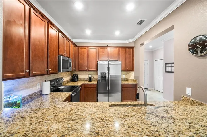 Kitchen featuring tasteful backsplash, stainless steel appliances, sink, light stone counters, and crown molding