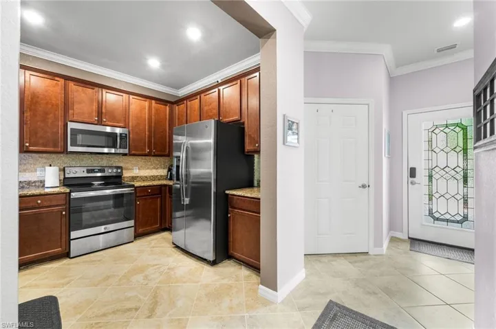 Kitchen with light tile patterned flooring, stainless steel appliances, crown molding, light stone counters, and backsplash
