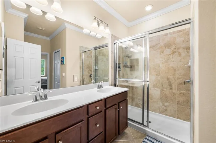 Bathroom featuring a shower with shower door, tile patterned floors, crown molding, and double vanity