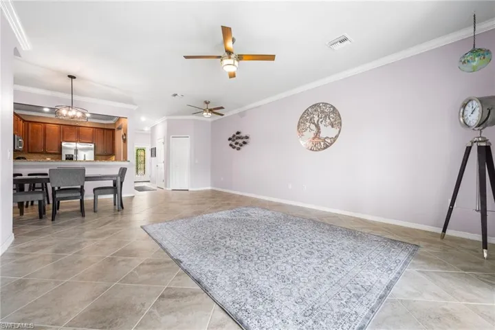 Living room featuring crown molding, ceiling fan with notable chandelier, and light tile patterned floors