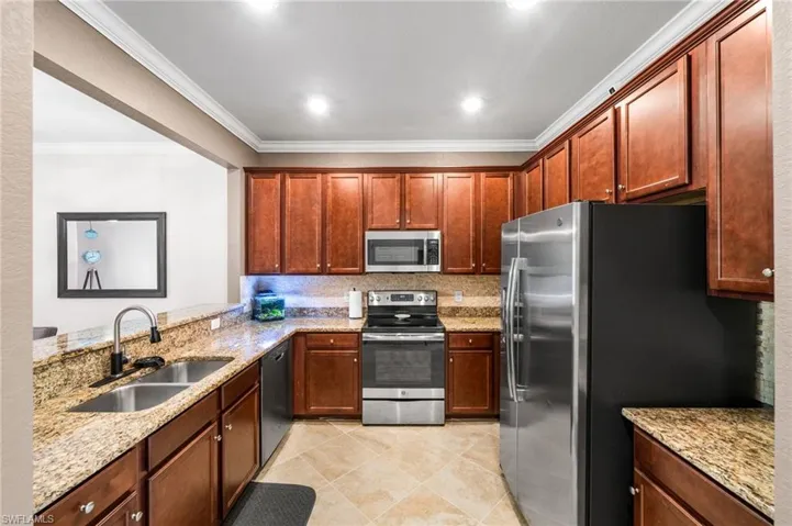 Kitchen featuring light tile patterned floors, light stone countertops, appliances with stainless steel finishes, sink, and ornamental molding