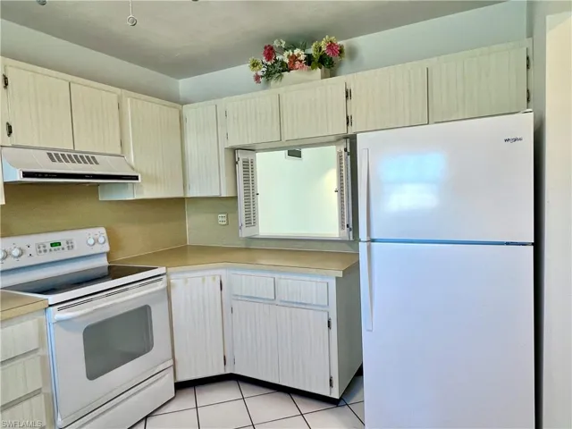 Kitchen with white appliances, light countertops, light tile patterned floors, and exhaust hood