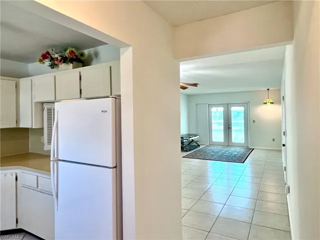 Kitchen with freestanding refrigerator, french doors, light tile patterned floors, white cabinetry, and light countertops