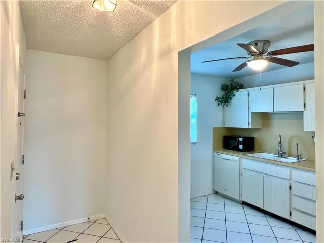 Kitchen with light countertops, white cabinets, light tile patterned floors, a ceiling fan, and a textured ceiling