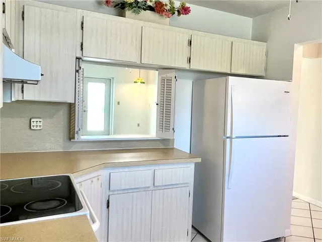 Kitchen with freestanding refrigerator, light countertops, light tile patterned flooring, range hood, and electric stovetop